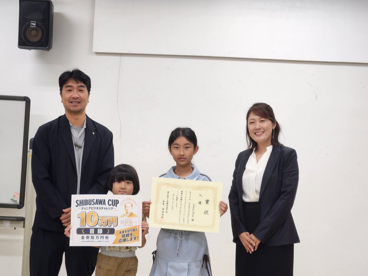 産業祭出店権を獲得したHAPICOの表彰。実践予算10万円のボードと賞状を手にする小学生